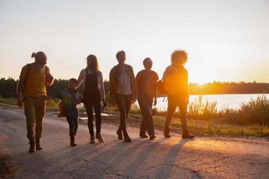 Large group of six family members of different ages and nationalities walks along a forest road against the backdrop of sunset,people walk with backpacks looking for picnic spot, high quality photo