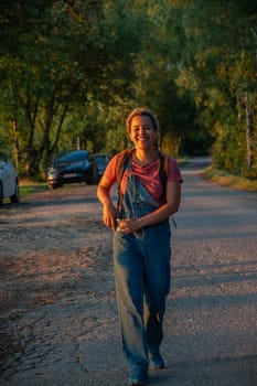 A young Brazilian woman in denim overalls walks along a forest road, the girl smiles happily,there is a car in the background, High quality photo