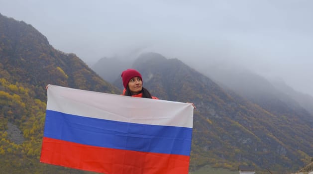 Close-up of the Russian flag fluttering beautifully in the hands of a woman against the backdrop of the Caucasus Mountains on a cloudy foggy day. Russian Independence Day.