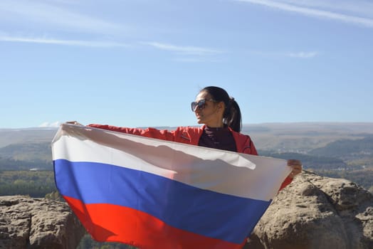 The Russian flag is on the shoulders of a girl standing against the backdrop of the Caucasus mountains. Unity Day in Russia