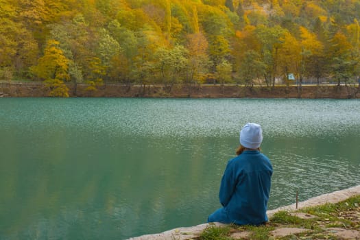 A lonely woman sits on the shore of a mountain forest lake. Autumn landscape, tranquility, tranquility, travel