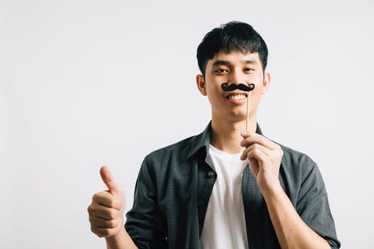 An Asian man's portrait features a playful expression as he holds a funny mustache card, radiating happiness and humor. Isolated on white for Fathers Day and November concept.