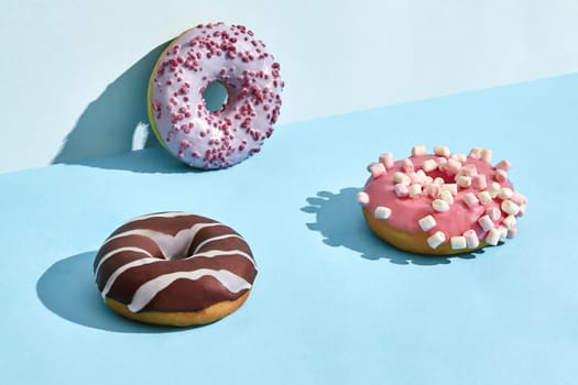 Close up photo of three sweet tasty donuts in caramel and chocolate icing, on a blue background. Mock up, two-colored pastel