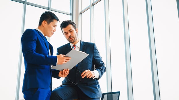 Two business people talk project strategy at office meeting room. Businessman discuss project planning with colleague at modern workplace while having conversation and advice on financial report. Jivy