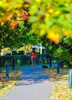 A woman walks her dog along the sidewalk in a city park on a sunny day