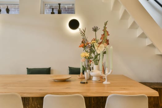 some flowers in a vase on a wooden table with white chairs and an open staircase leading up to the second floor