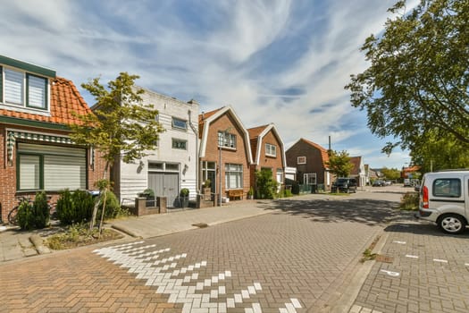 an empty street in the middle of a small town with parked cars and houses on both sides, under a cloudy blue sky