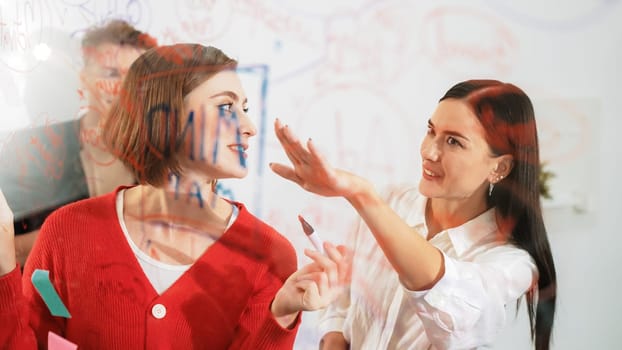 Professional business team brainstorming and working together about marketing project. Female caucasian leader writing idea on stick note while coworker present her idea confidently. Immaculate.