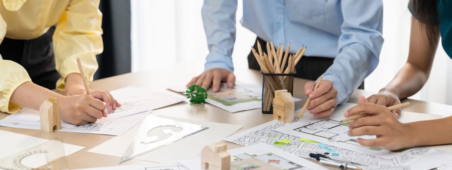 A portrait of professional architect team discussion about architectural project on meeting table with blueprint and wooden block scatter around at modern office. Closeup. Focus hand. Delineation.