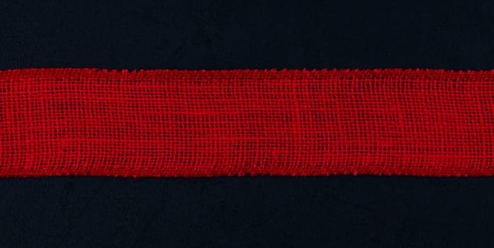 Red baggy ribbon lies in the middle on a black background with space for text on the sides, top view close-up. Concept black friday, valentine day, detective.