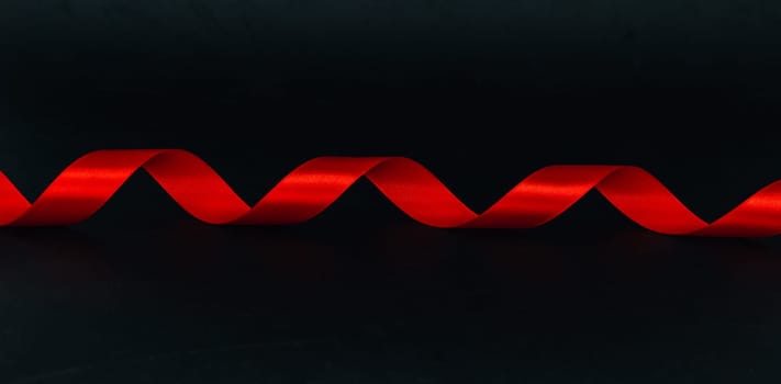 Red spiral ribbon lies in the middle on a black background with space for text on the sides, close-up side view. Concept of black friday, christmas, detective and mystic.