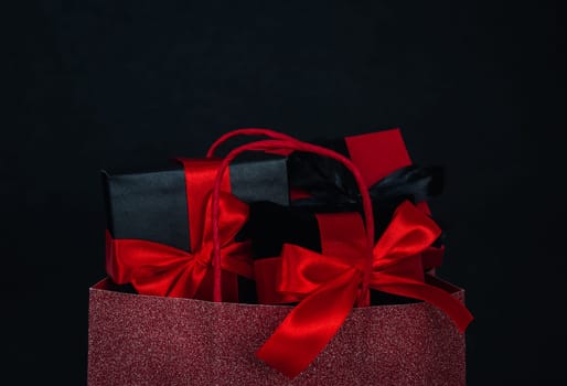 One red shiny bag with three gift boxes on a black background with place for text, close-up side view. Christmas and black friday concept.