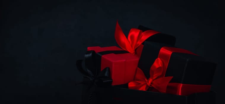 One paper bag with three gift boxes on the right against a black background with space for text on the left, close-up side view. Christmas and black friday concept.