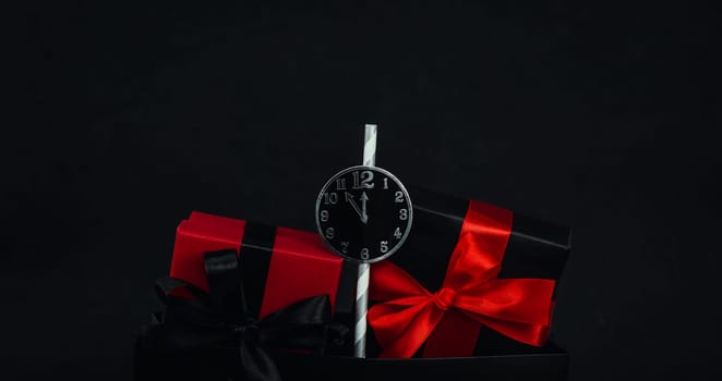 One package with three gift boxes and a paper clock in the middle on a black background with space for text, close-up side view. Christmas and black friday concept.