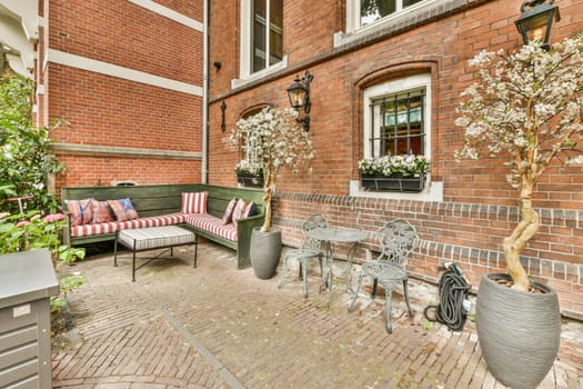 an outside area with furniture and flowers on the side of a brick building, in front of a green bench