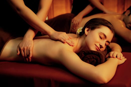 Caucasian couple customer enjoying relaxing anti-stress spa massage and pampering with beauty skin recreation leisure in warm candle lighting ambient salon spa at luxury resort or hotel. Quiescent