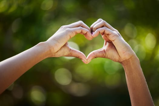 Hands, heart as a symbol or love or health with a person outdoor in nature on a blurred background for sustainability. Like, romance or valentines day with green gesture in a garden or yard in summer.