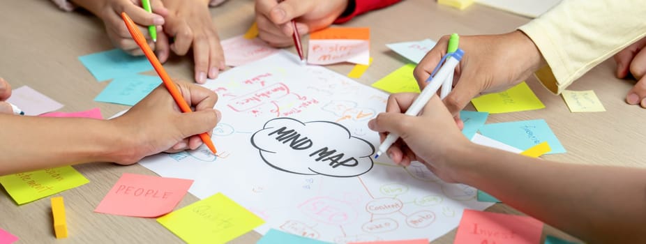 Professional startup group share creative marketing idea by using mind map. Young skilled business people brainstorm business plan while writing sticky notes. Focus on hand. Closeup. Variegated.