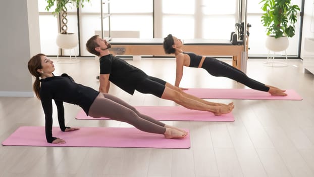 Two women and a man are doing yoga in the studio