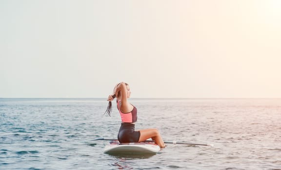 Silhouette of woman standing, surfing on SUP board, confident paddling through water surface. Idyllic sunset or sunrise. Sports active lifestyle at sea or river.