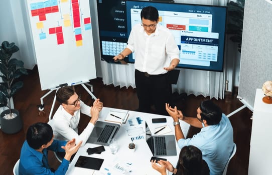 Project manager communicate and collaborate with team using project management software display on monitor, tracking progress of project task and making schedule plan at meeting table. Prudent