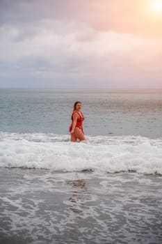 Woman in a bathing suit at the sea. A fat young woman in a red swimsuit enters the water during the surf.