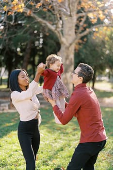 Parents lift a little smiling girl up by her arms and legs. High quality photo