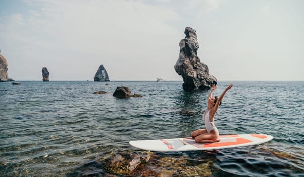 Woman sup yoga. Middle age sporty woman practising yoga pilates on paddle sup surfboard. Female stretching doing workout on sea water. Modern individual hipster outdoor summer sport activity