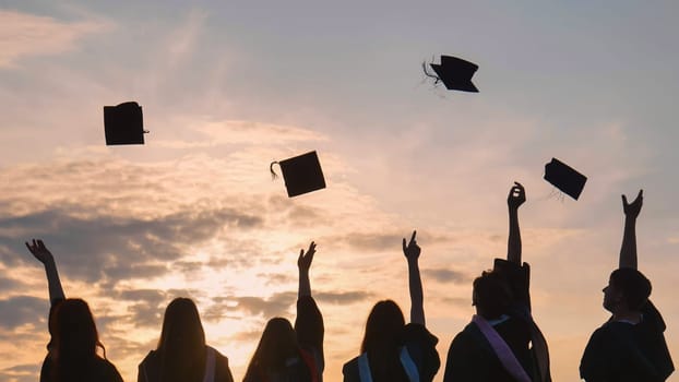 Student graduates toss their caps at sunset