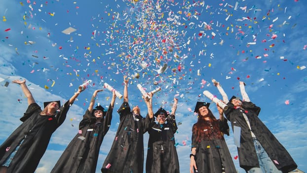 Graduates throw colorful confetti against a blue sky