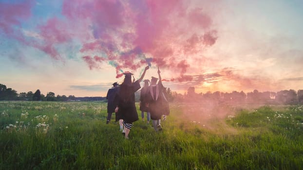 Students graduate with colored smoke walking through the meadow in the evening