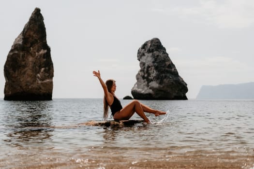 Woman travel sea. Young Happy woman in a long red dress posing on a beach near the sea on background of volcanic rocks, like in Iceland, sharing travel adventure journey