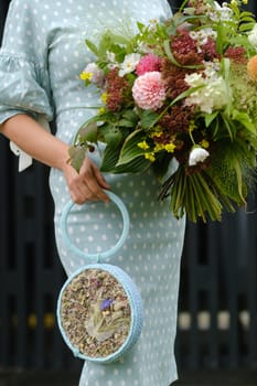 A round blue handbag with a decor of flowers and a bouquet in the girl's hand.