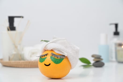 An orange fruit with towel and patches under eyes. Spa treatment and self care concept.