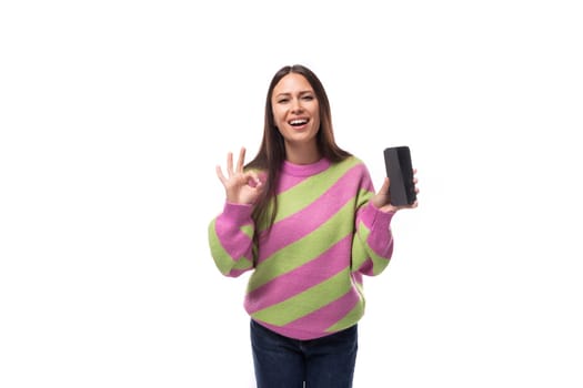 beautiful young brunette woman in a striped pink blouse shows the screen of a smartphone with a mockup on a white background with copy space.