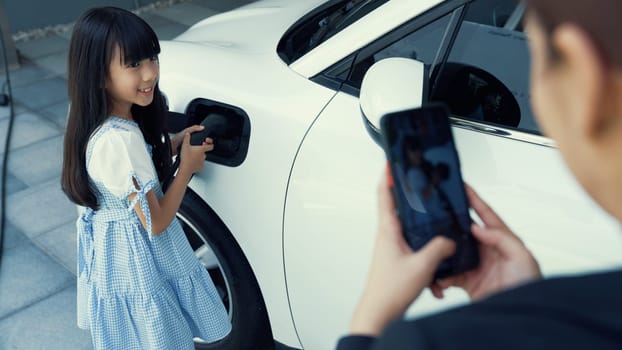 Progressive lifestyle of mother and daughter who have just returned from school in an electric vehicle that is being charged at home. Electric vehicle powered by sustainable clean energy.