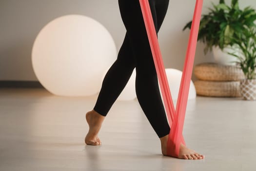 Close-up of the legs of a Girl in black doing fitness with red ribbons indoors.