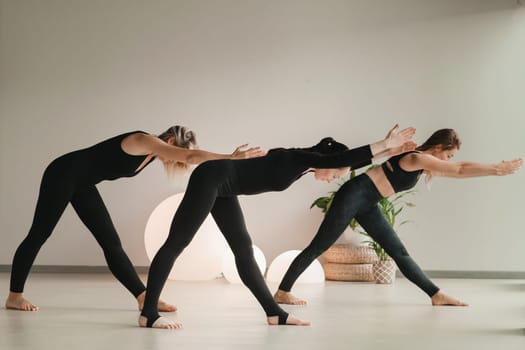 A group of girls in black doing yoga poses indoors. Women are engaged in fitness.