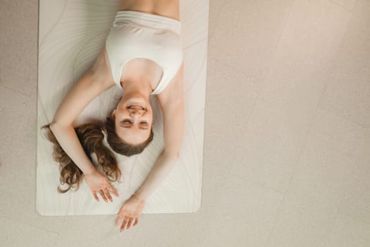 A girl in white clothes lies on a rug and laughs before yoga classes indoors.