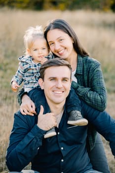 Smiling mother hugs a little girl from behind on her father shoulders. Portrait. High quality photo