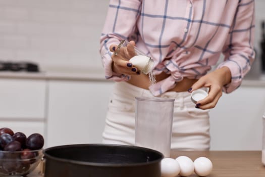 woman preparing pie in modern kitchen, adding ingredients to bowl