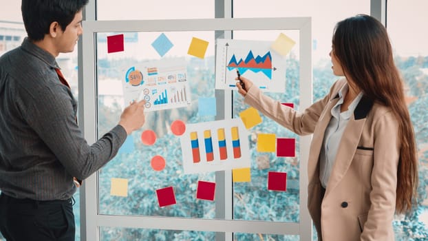 Business people work on project planning board in office and having conversation with coworker friend to analyze project development . They use sticky notes posted on glass to make it organized. Jivy