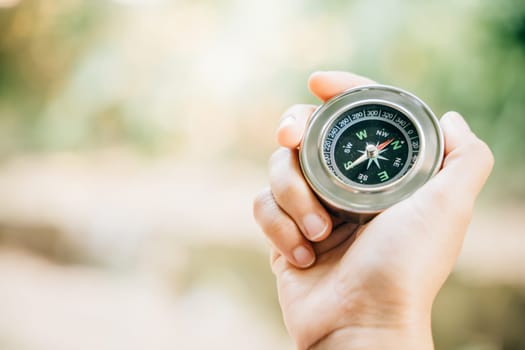 Hiker searches for direction in the forest holding a compass to overcome confusion. The compass in the hand signifies exploration and finding one way in the wilderness.