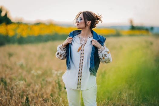 Smiling attractive hippy woman on nature background. Young lady in white embroidery shirt, denim waistcoat. Summer fashion, hipster, ethno, folk lifestyle.