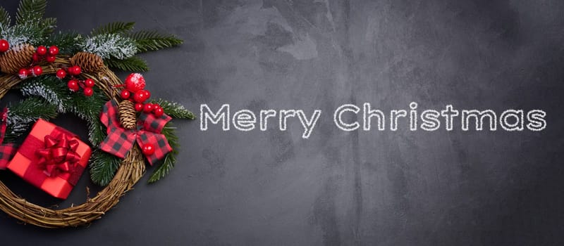 A circular Christmas wreath made of fir branches and other decorations on a black chalkboard, Merry Christmas inscription