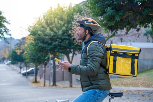 Delivery man on bike looking GPS location in the phone. Black courier delivering food and drink in town outdoors on stylish bicycle. High quality photo