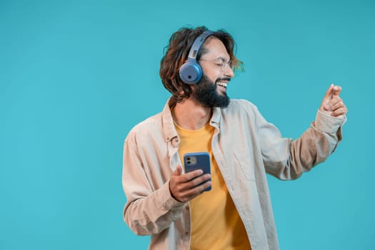 Happy man dancing isolated on blue background with headphones and smartphone. High quality photo