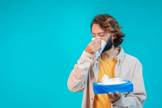 Man blowing out nose with napkin isolated on blue. Winter cold concept. High quality photo