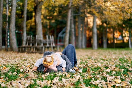 Little girl lies on her mother stomach on the autumn lawn, hugging her. High quality photo