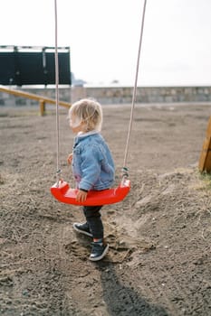 Little girl stands near a rope swing on the playground and looks away. High quality photo